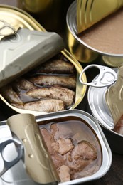 Photo of Open tin cans with different preserved products on table, closeup