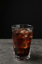 Photo of Cold cola with ice cubes in glass on grey table against black background. Space for text