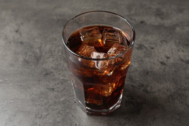 Photo of Cold cola with ice cubes in glass on grey table, closeup