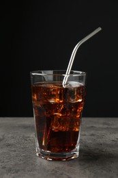 Photo of Cold cola with ice cubes and drinking straw in glass on grey table against black background