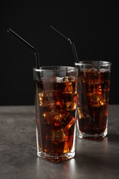 Photo of Cold cola with ice cubes and drinking straws in glasses on grey table against black background, closeup