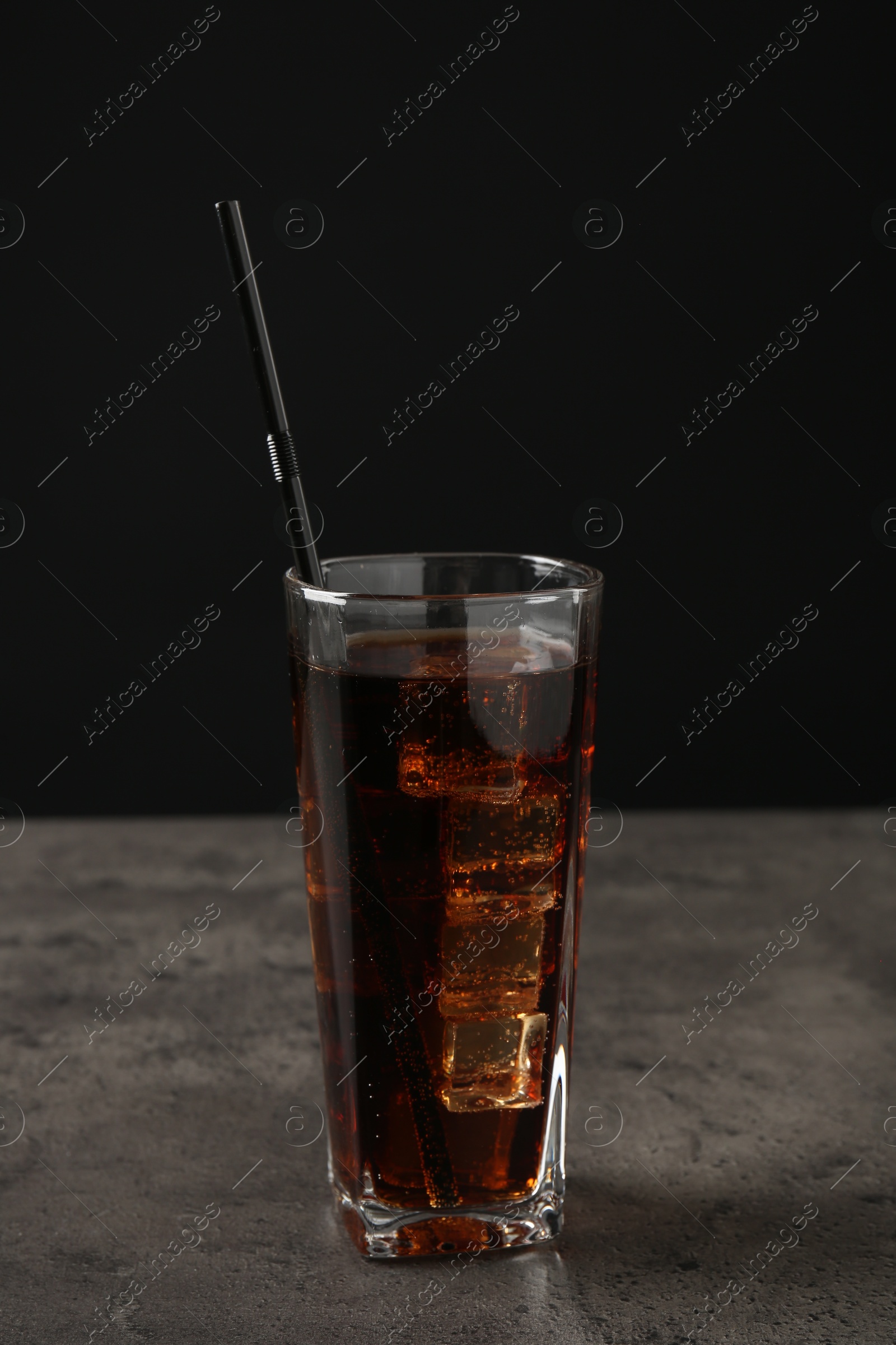 Photo of Cold cola with ice cubes and drinking straw in glass on grey table against black background. Space for text