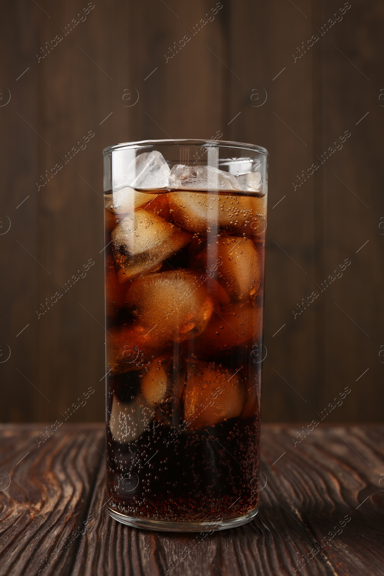 Photo of Cold cola with ice cubes in glass on wooden table, closeup