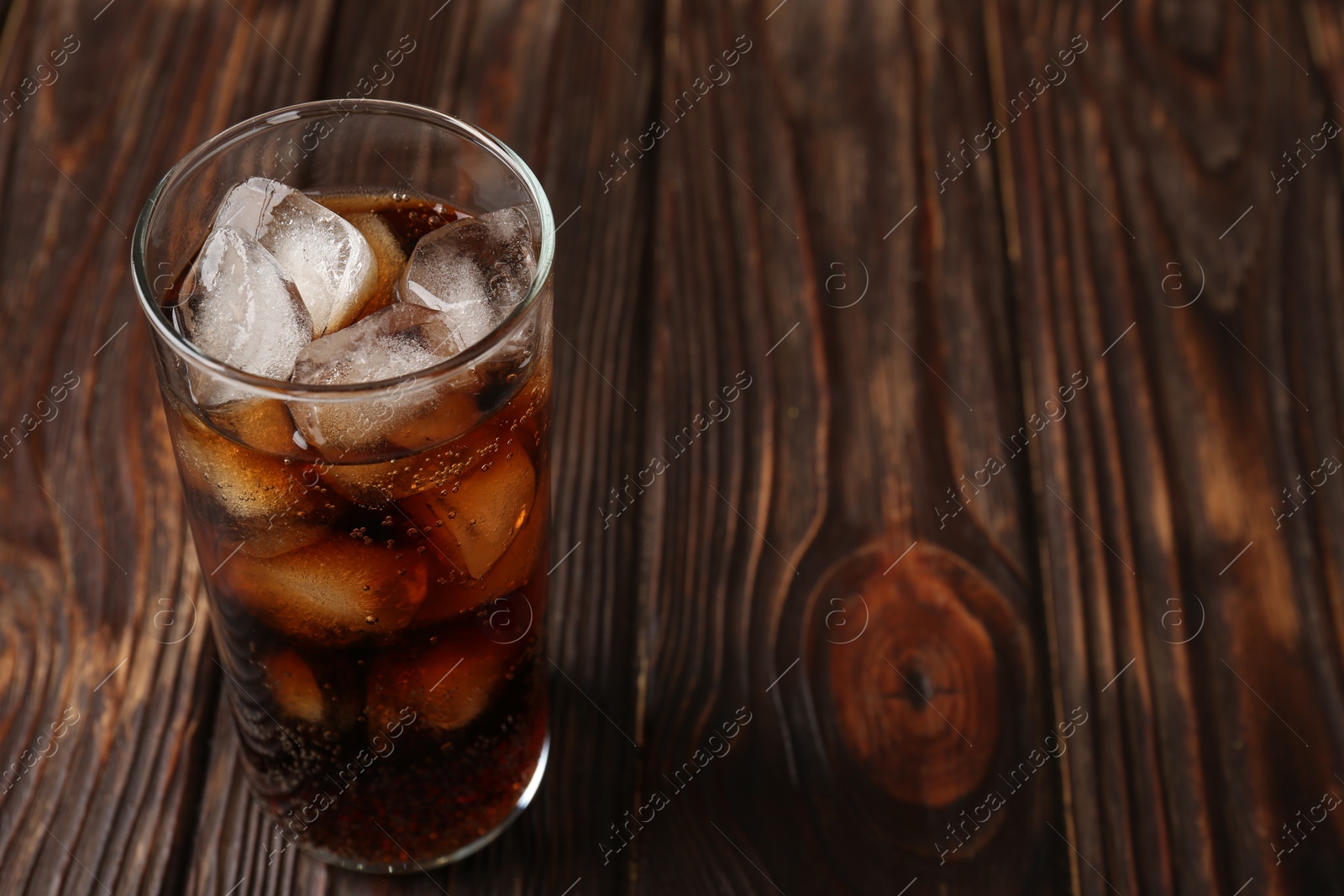 Photo of Cold cola with ice cubes in glass on wooden table. Space for text