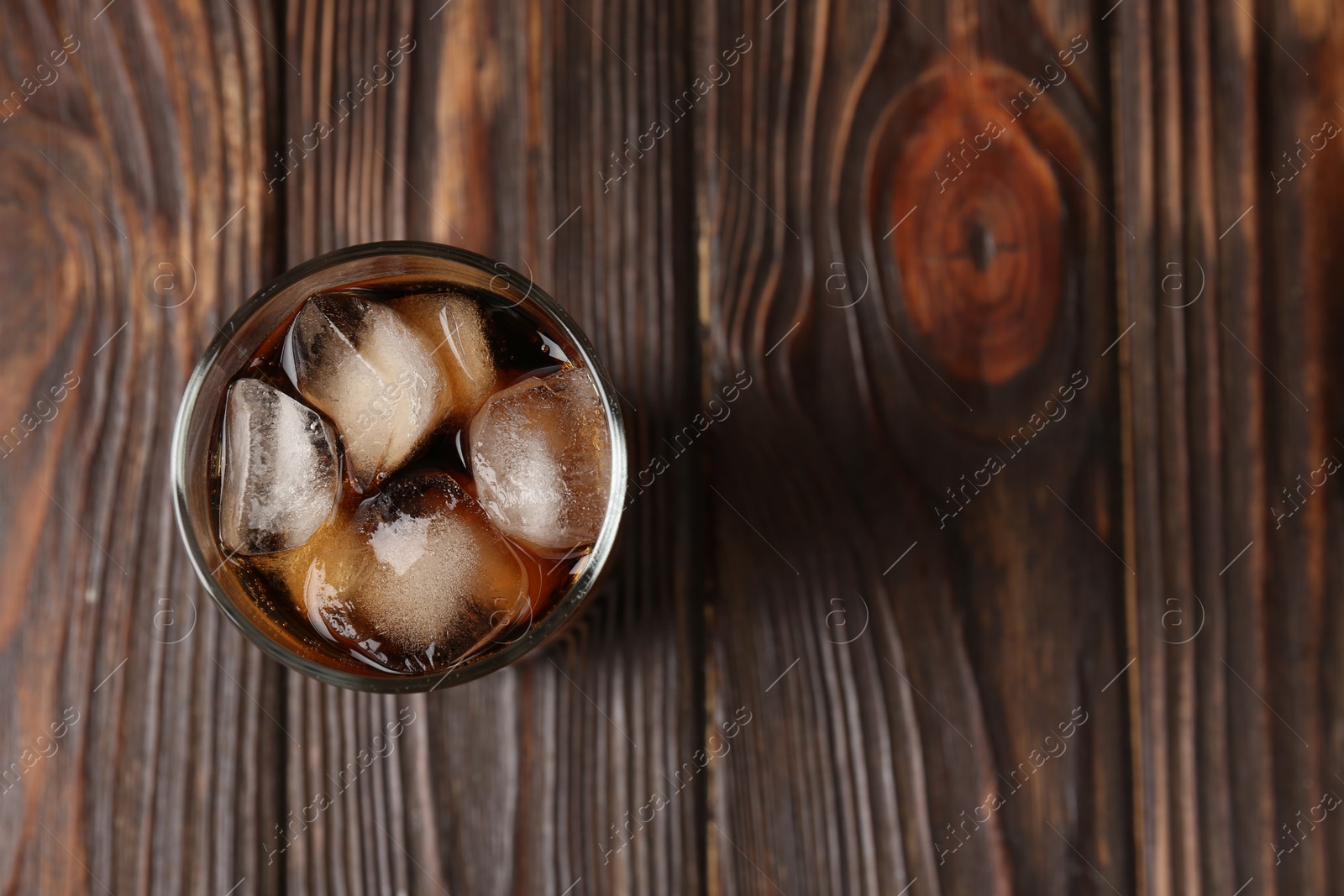 Photo of Cold cola with ice cubes in glass on wooden table, top view. Space for text