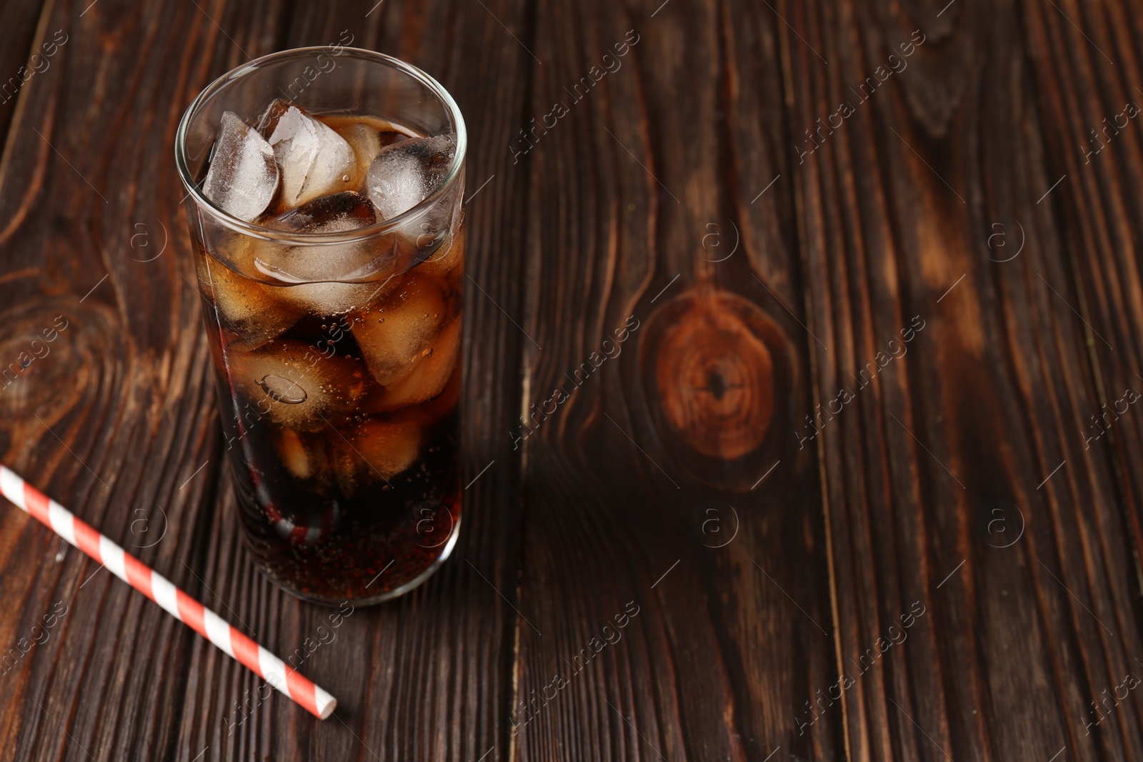 Photo of Cold cola with ice cubes in glass and drinking straw on wooden table. Space for text