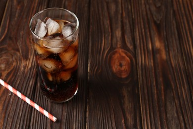 Photo of Cold cola with ice cubes in glass and drinking straw on wooden table. Space for text