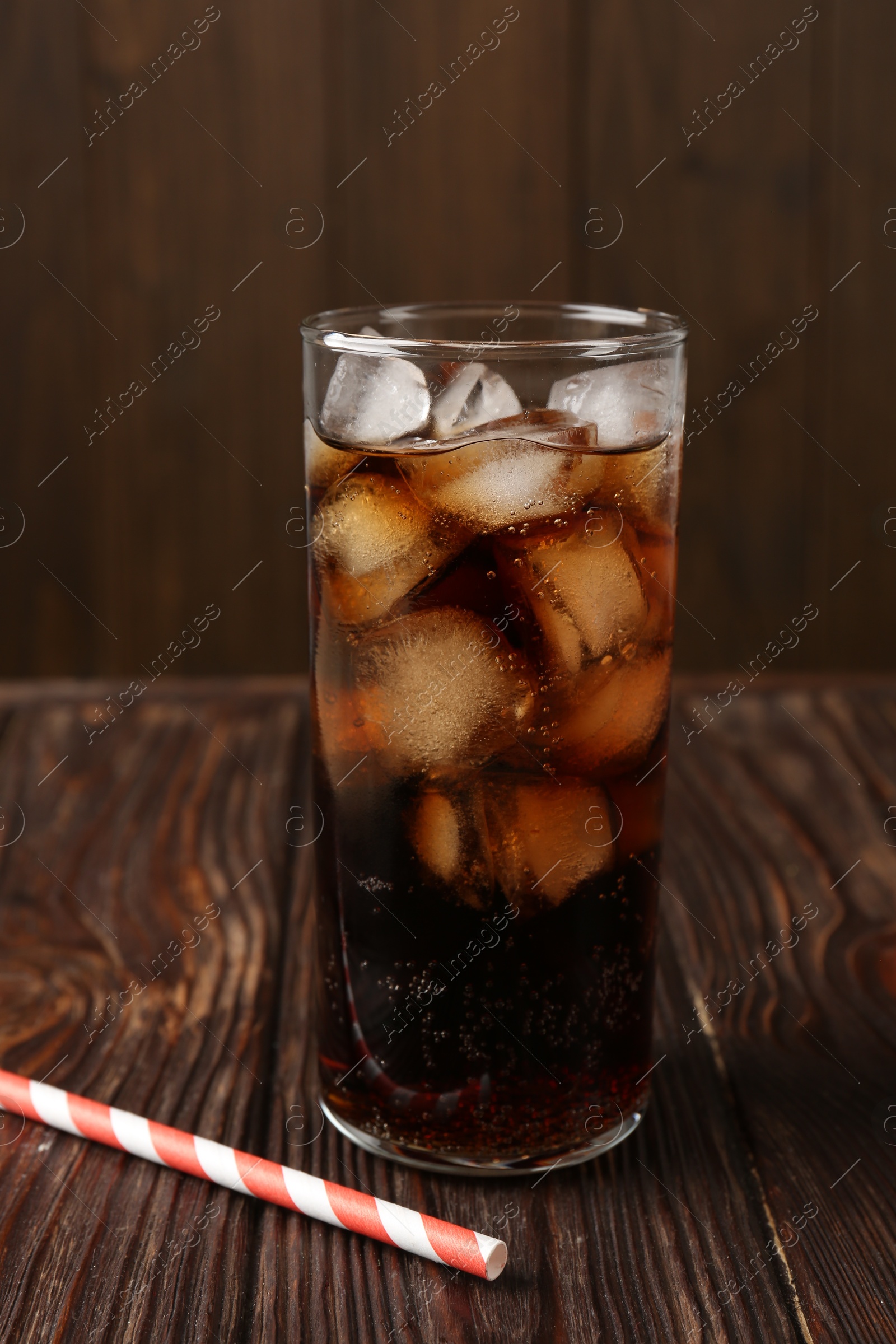 Photo of Cold cola with ice cubes in glass and drinking straw on wooden table