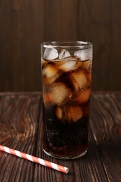 Photo of Cold cola with ice cubes in glass and drinking straw on wooden table