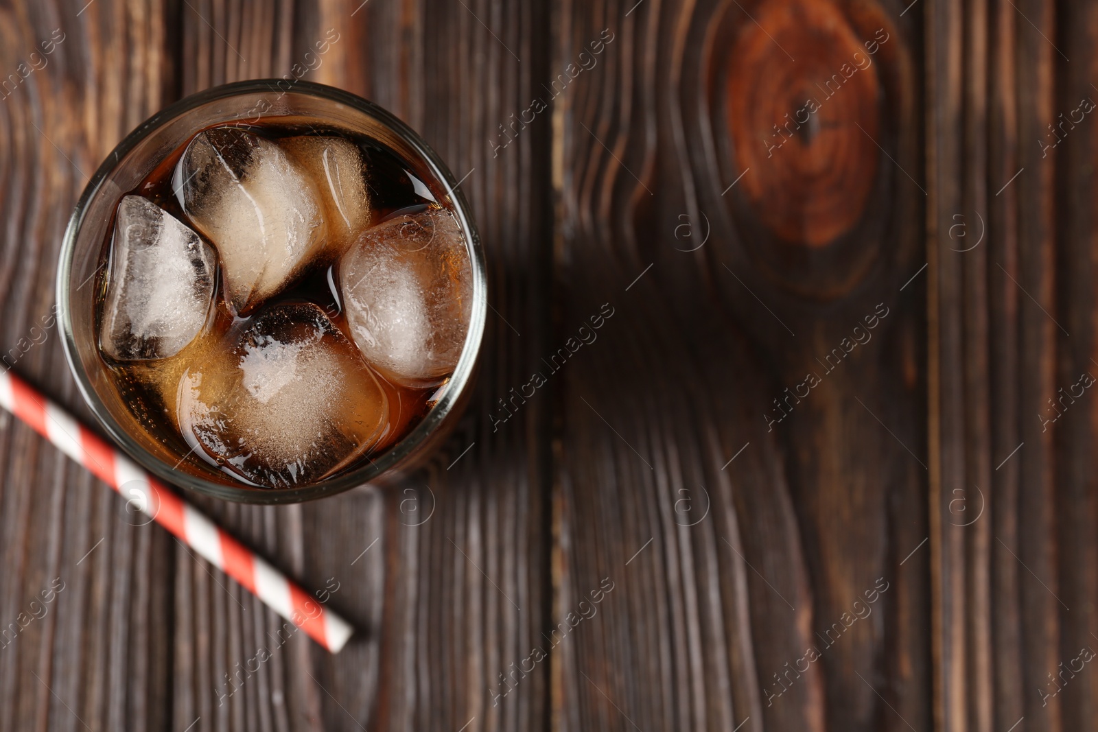 Photo of Cold cola with ice cubes in glass and drinking straw on wooden table, top view. Space for text