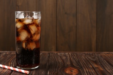 Photo of Cold cola with ice cubes in glass and drinking straw on wooden table. Space for text