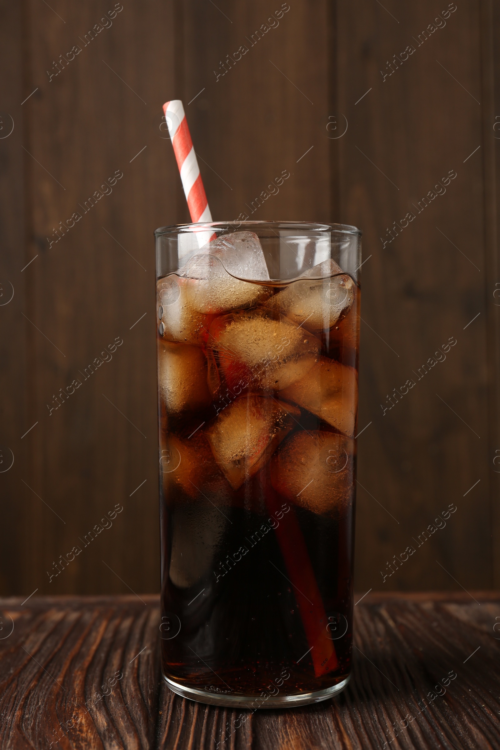 Photo of Cold cola with ice cubes and drinking straw in glass on wooden table