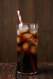 Photo of Cold cola with ice cubes and drinking straw in glass on wooden table