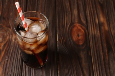 Photo of Cold cola with ice cubes and drinking straw in glass on wooden table. Space for text