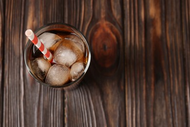 Photo of Cold cola with ice cubes and drinking straw in glass on wooden table, top view. Space for text