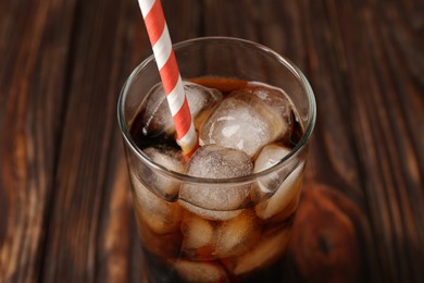 Photo of Cold cola with ice cubes and drinking straw in glass on wooden table, closeup