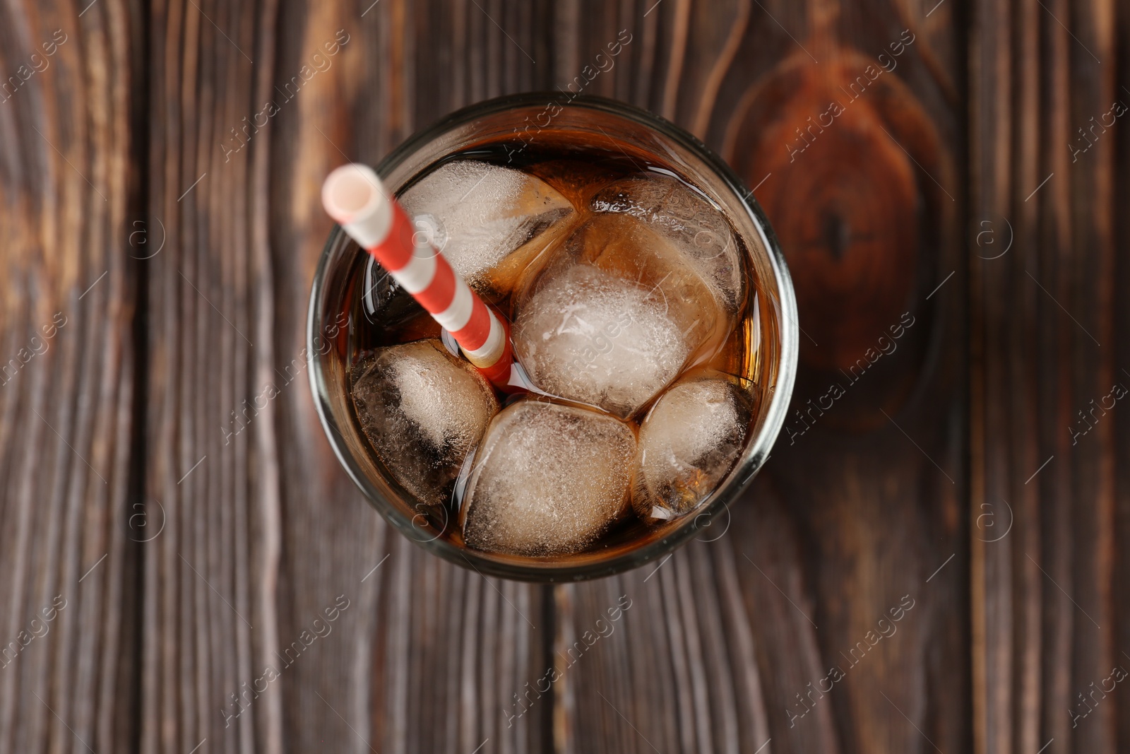 Photo of Cold cola with ice cubes and drinking straw in glass on wooden table, top view