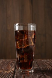 Photo of Cold cola with ice cubes in glass on wooden table