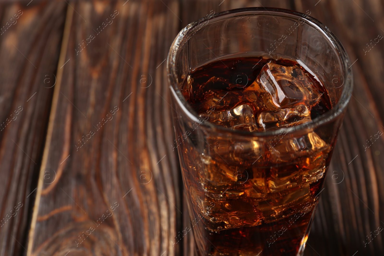 Photo of Cold cola with ice cubes in glass on wooden table, closeup. Space for text