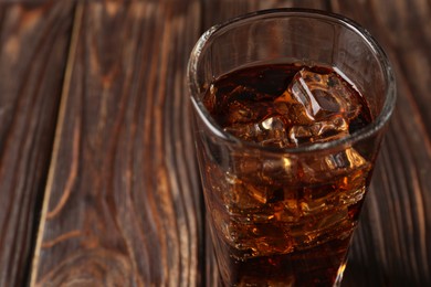 Photo of Cold cola with ice cubes in glass on wooden table, closeup. Space for text