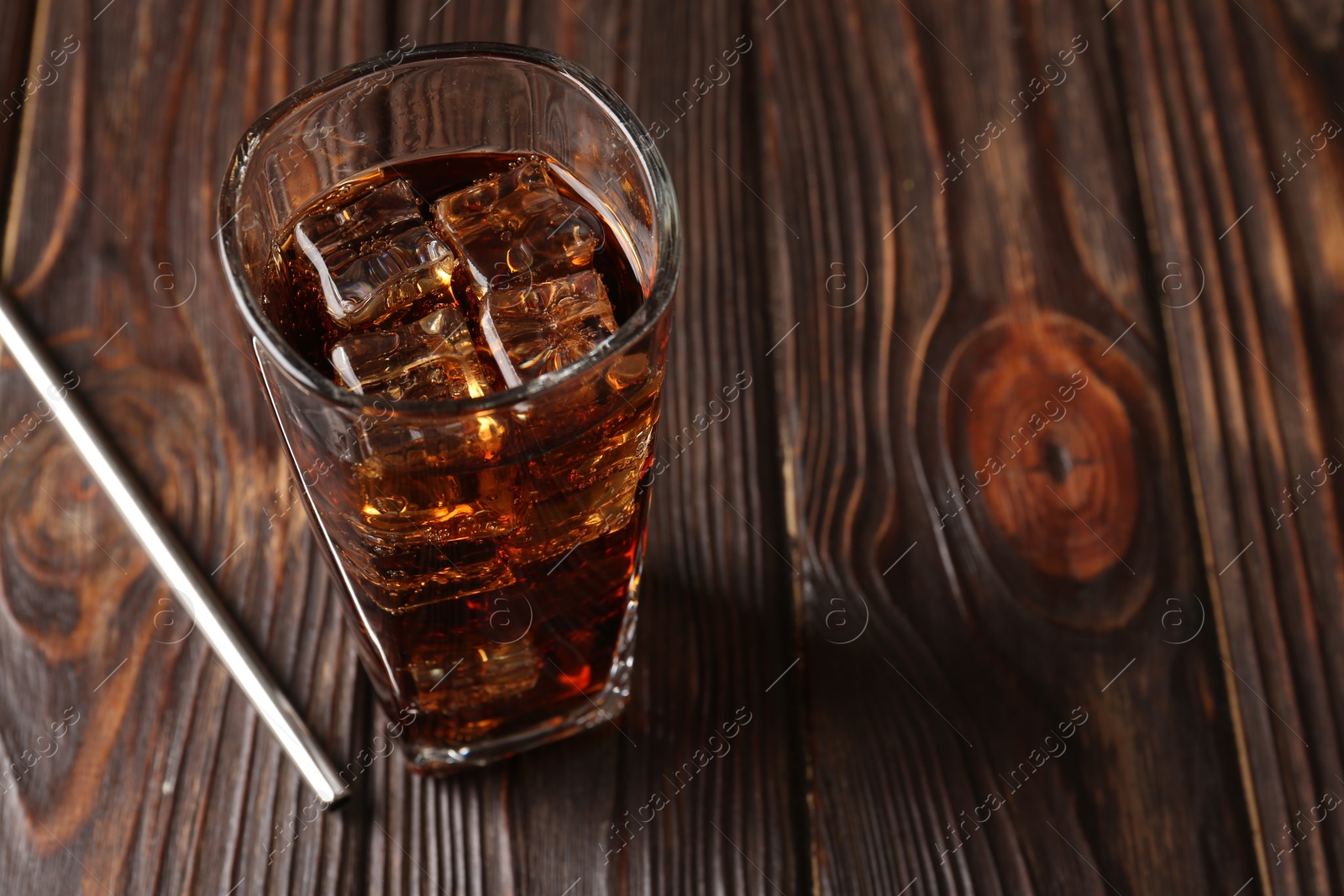 Photo of Cold cola with ice cubes in glass and drinking straw on wooden table. Space for text