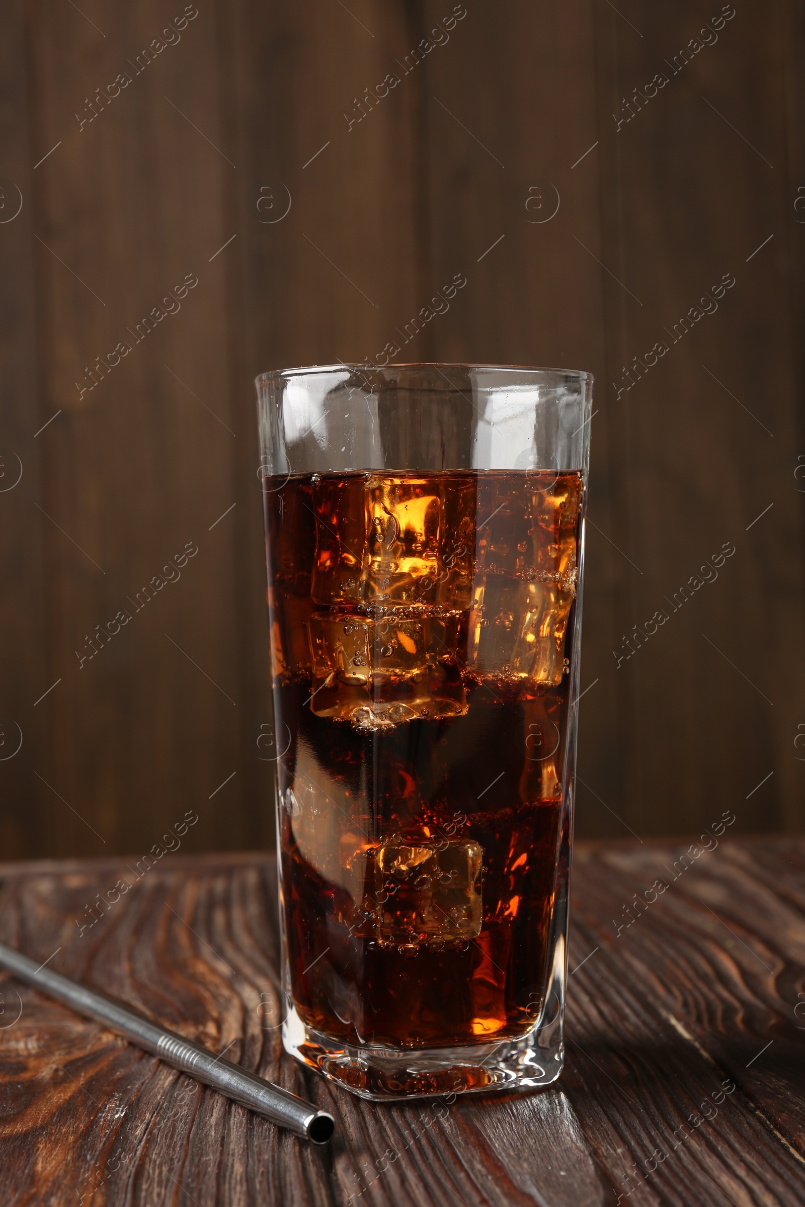 Photo of Cold cola with ice cubes in glass and drinking straw on wooden table