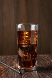 Photo of Cold cola with ice cubes in glass and drinking straw on wooden table