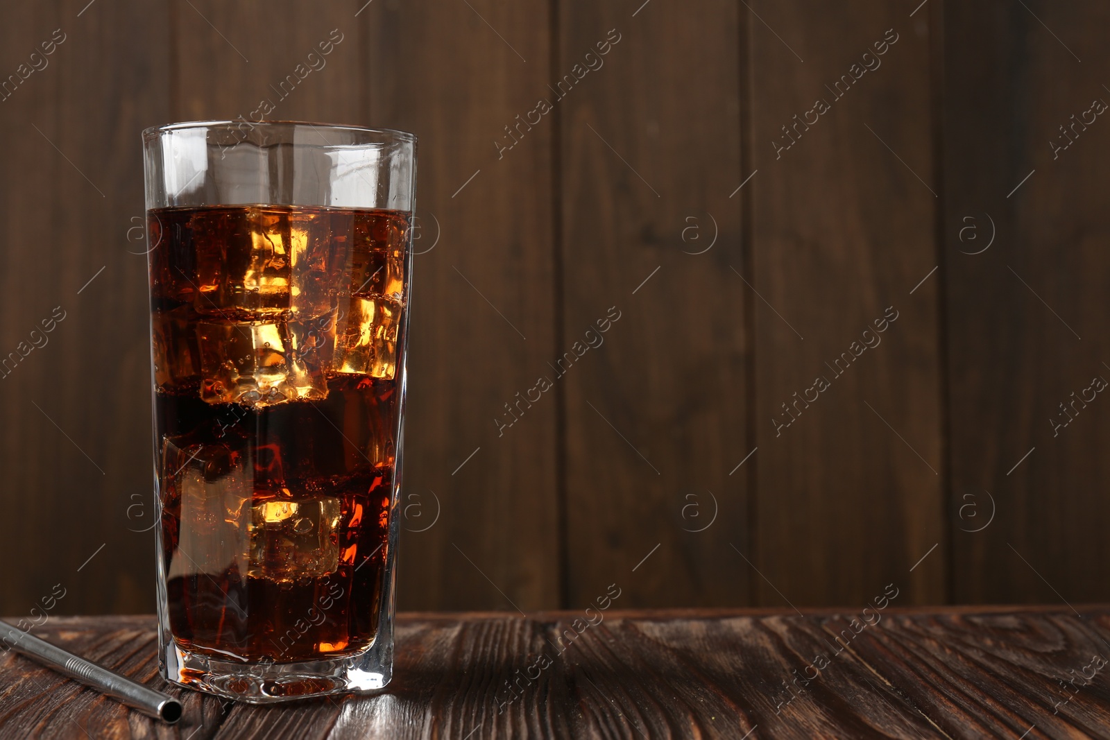 Photo of Cold cola with ice cubes in glass and drinking straw on wooden table. Space for text