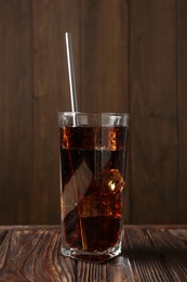 Photo of Cold cola with ice cubes and drinking straw in glass on wooden table