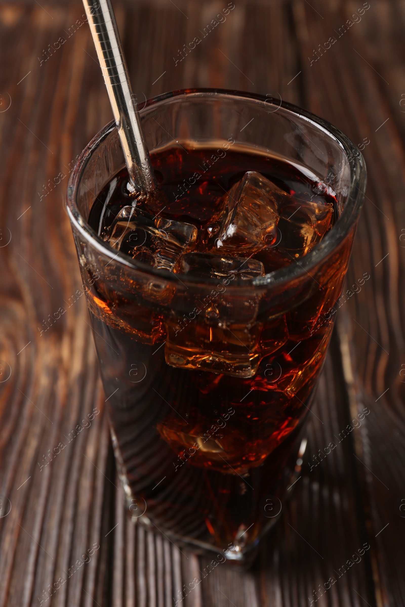 Photo of Cold cola with ice cubes and drinking straw in glass on wooden table, closeup