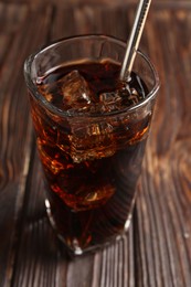 Photo of Cold cola with ice cubes and drinking straw in glass on wooden table, closeup