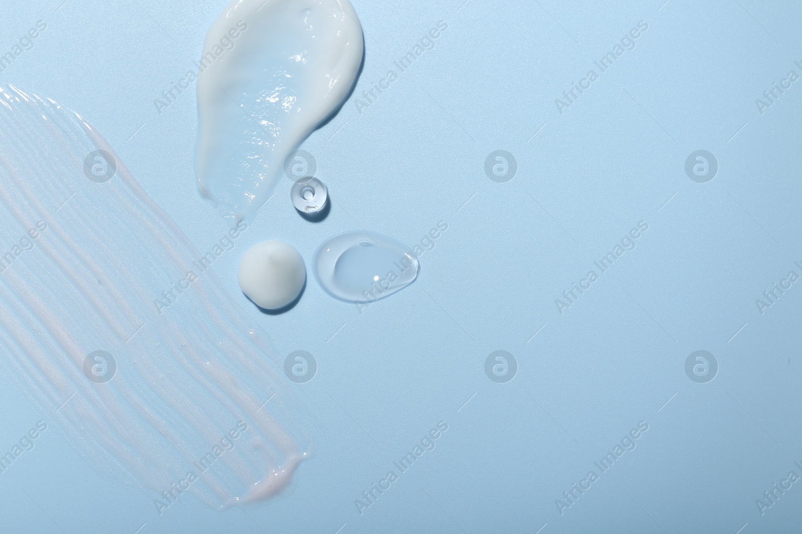 Photo of Cream and gel samples on light blue background, top view. Space for text