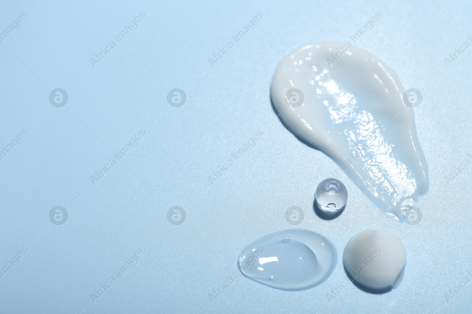 Photo of Cream and gel samples on light blue background, closeup. Space for text