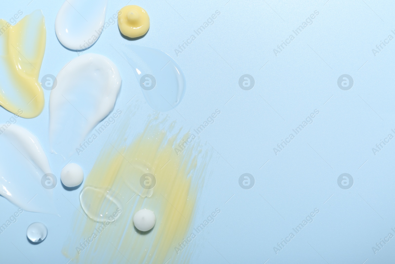 Photo of Cream and gel samples on light blue background, top view. Space for text