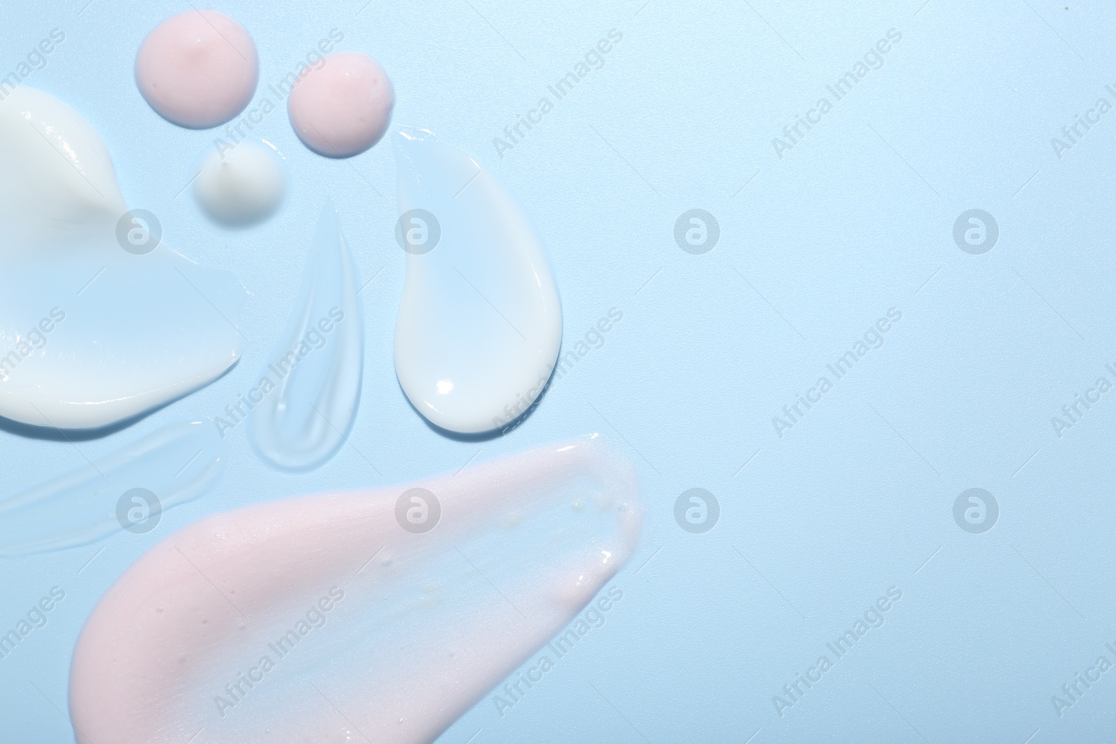 Photo of Cream and gel samples on light blue background, top view. Space for text