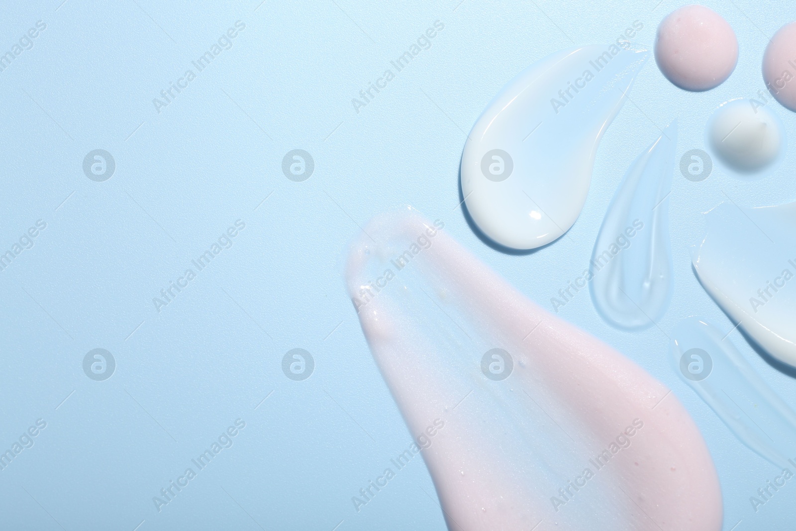 Photo of Cream and gel samples on light blue background, top view. Space for text