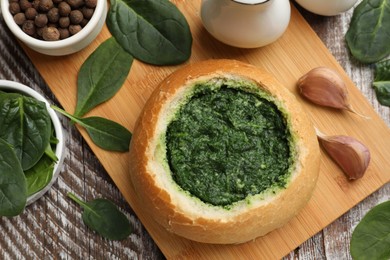 Delicious spinach sauce in bread bowl on wooden table, flat lay