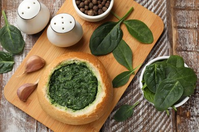 Photo of Delicious spinach sauce in bread bowl on wooden table, flat lay