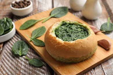 Delicious spinach sauce in bread bowl on wooden table, closeup