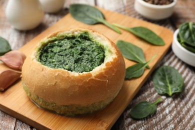 Delicious spinach sauce in bread bowl on wooden table, closeup