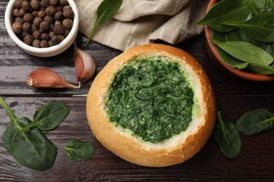 Delicious spinach sauce in bread bowl on wooden table, flat lay