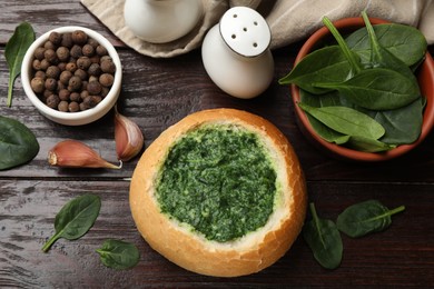 Delicious spinach sauce in bread bowl on wooden table, flat lay