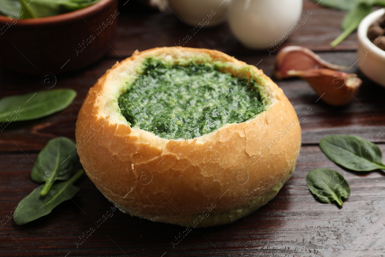 Photo of Delicious spinach sauce in bread bowl on wooden table, closeup