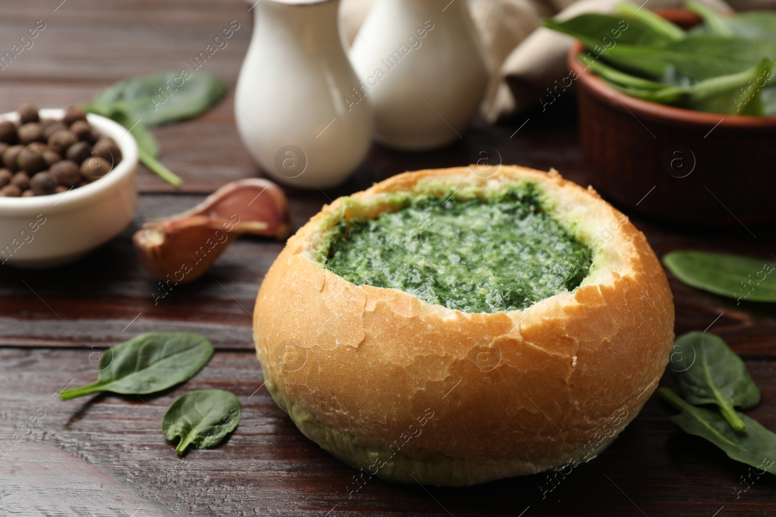 Photo of Delicious spinach sauce in bread bowl on wooden table, closeup