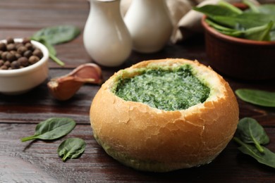 Photo of Delicious spinach sauce in bread bowl on wooden table, closeup