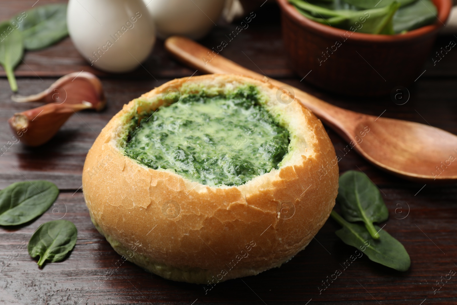 Photo of Delicious spinach sauce in bread bowl on wooden table, closeup