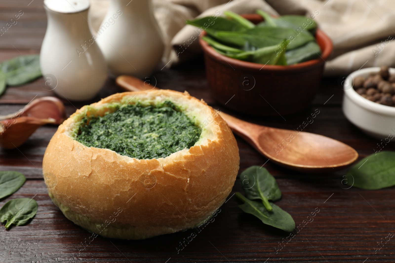 Photo of Delicious spinach sauce in bread bowl on wooden table, closeup