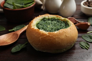 Photo of Delicious spinach sauce in bread bowl on wooden table, closeup