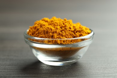 Photo of Turmeric powder in glass bowl on grey wooden table, closeup