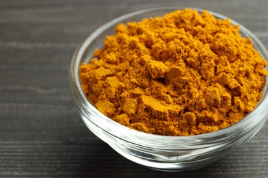 Photo of Turmeric powder in glass bowl on grey wooden table, closeup